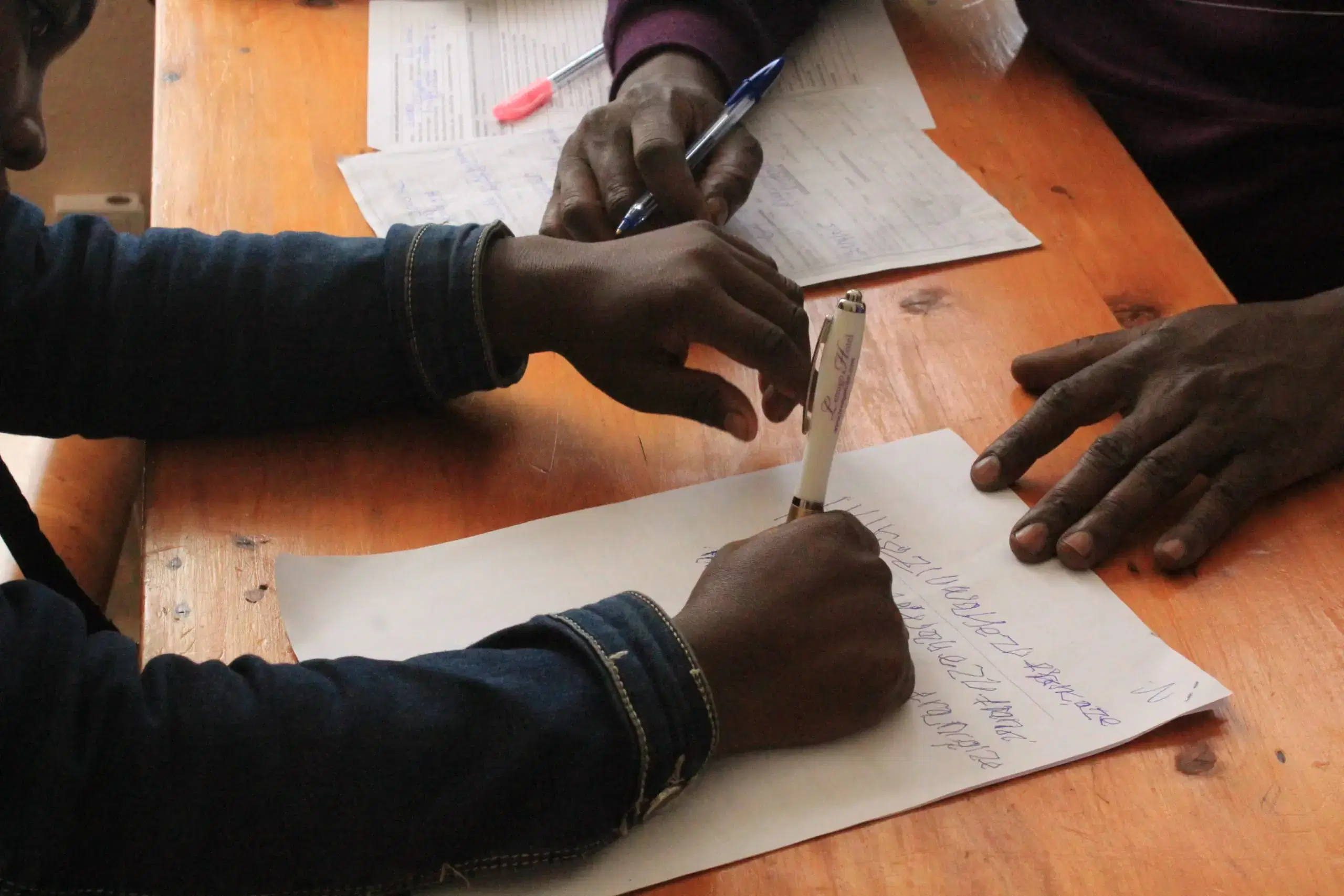 Close up of a child writing on paper on a desk in a classroom.